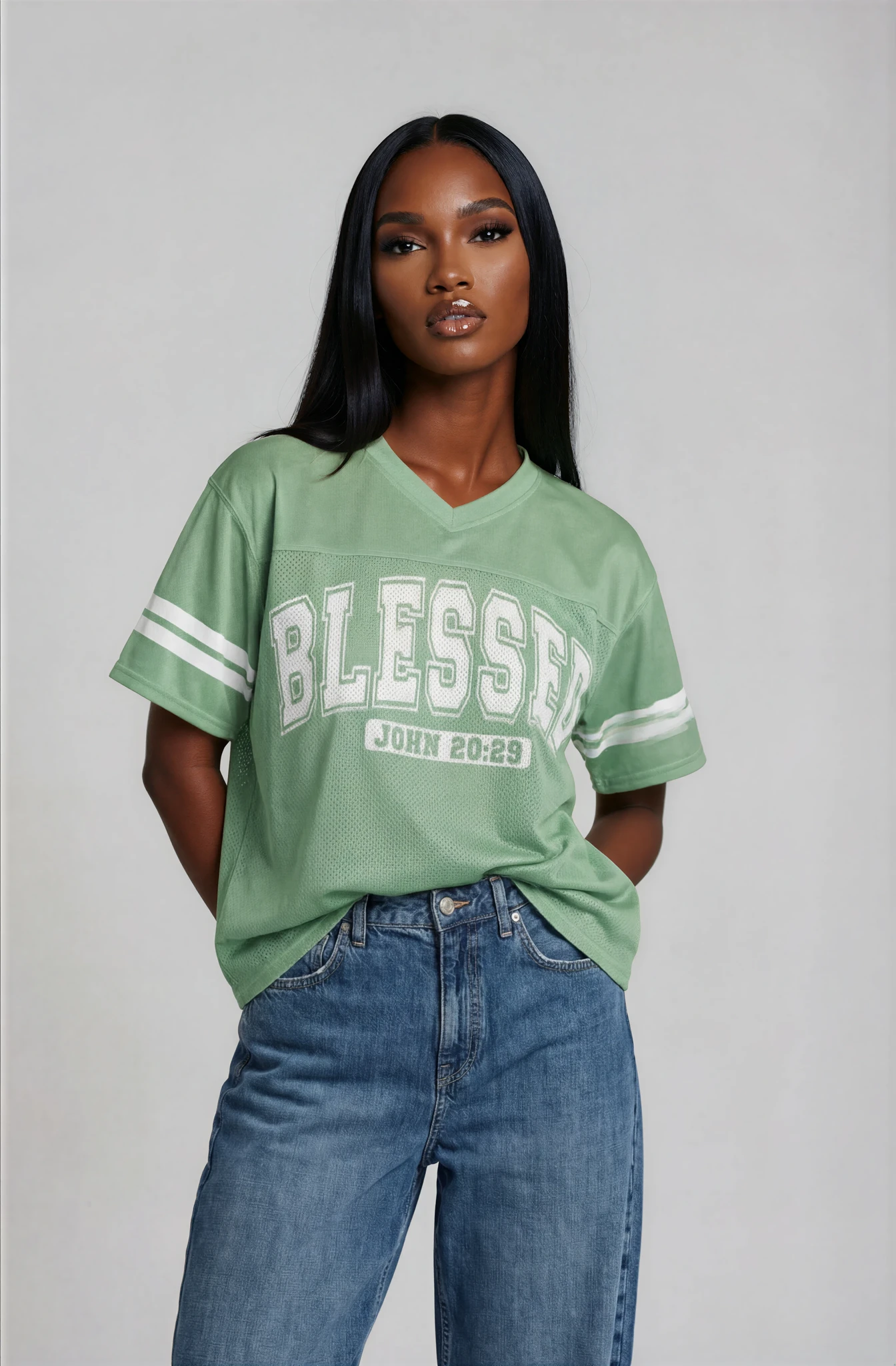 Woman wearing a green 'Blessed' t-shirt and blue jeans on a gray background